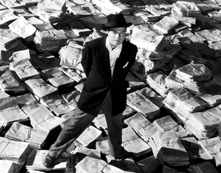 man wearing hat standing on pile of newspaper bundles